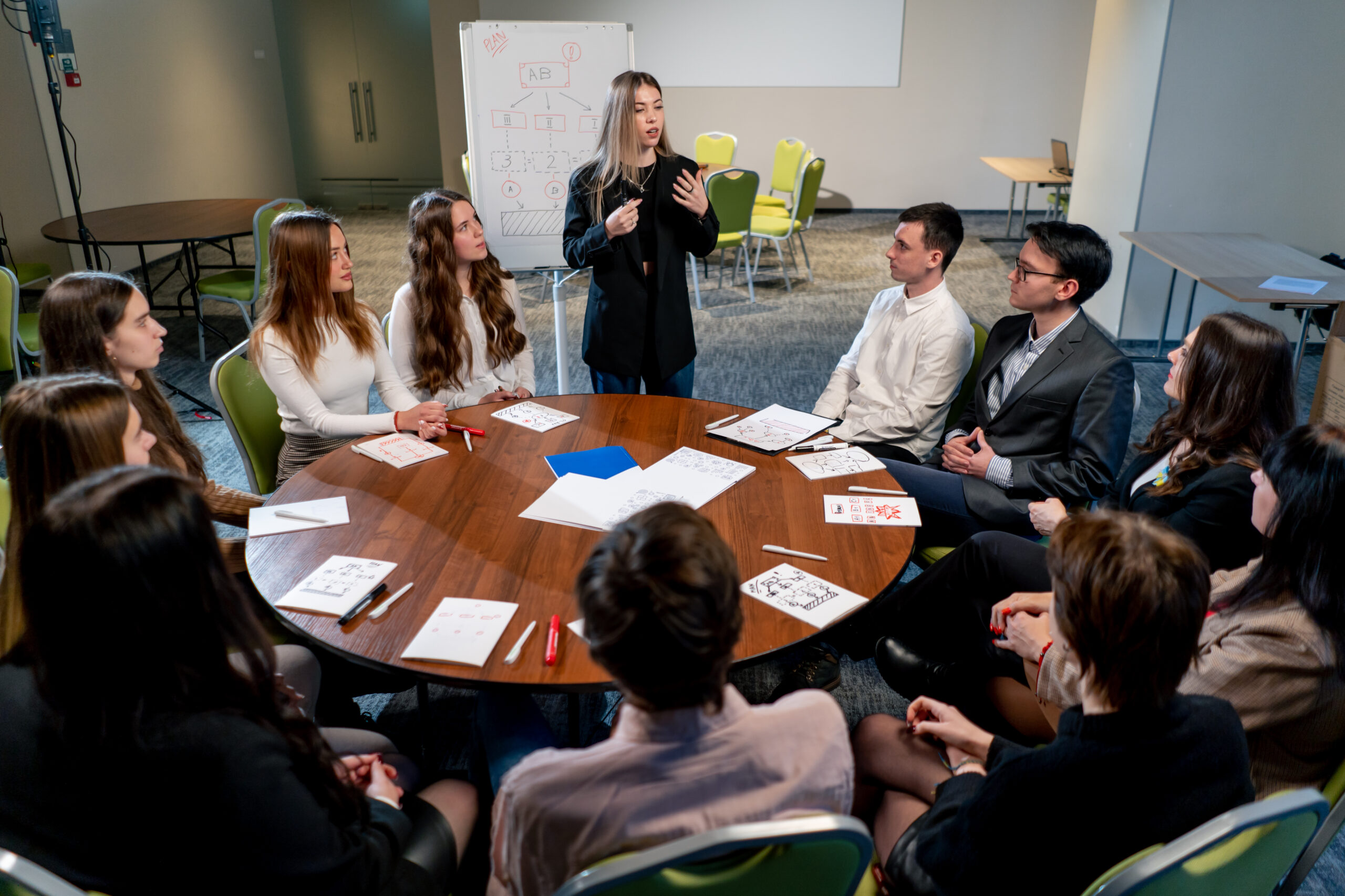 Students around a table discussing a topic. One woman stands while she speaks.