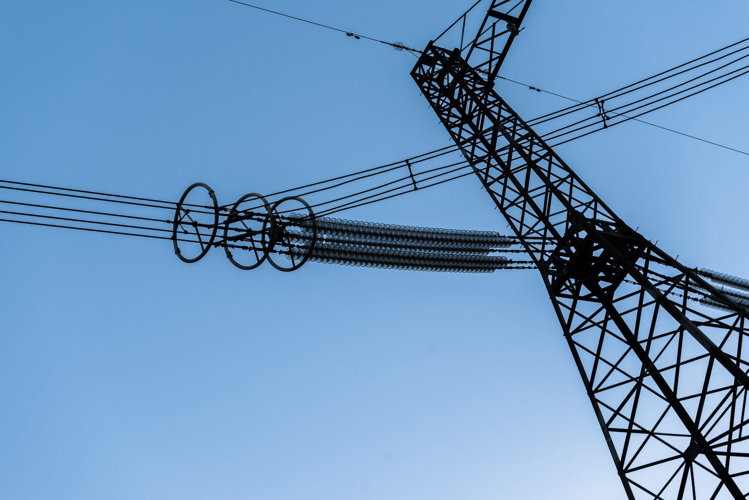 Silhouette of a high voltage power line under a blue sky.